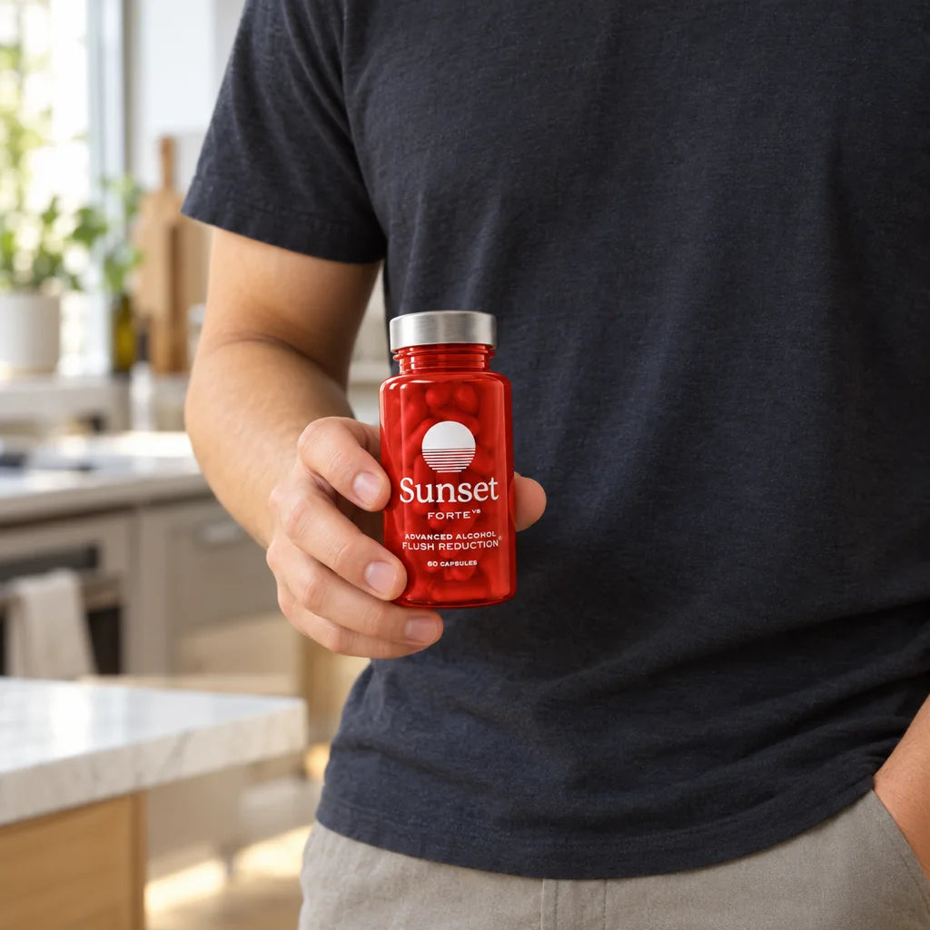 A man in a navy T-shirt holding a bottle of Sunset Forte at waist height in a kitchen
